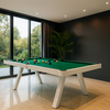 Moderne witte pooltafel met groen speelveld in een luxe ruimte met panoramische ramen, donkere muren, licht marmeren vloer en hoge kamerplant.