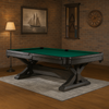 Luxe pooltafel met groene laken en donkerhouten onderstel, geplaatst op een vloerkleed in een sfeervolle mancave met bakstenen muur, wandklok, schilderij van een zeilschip, staande lamp en keurek met biljartaccessoires.